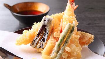 A plate of tempura with shrimp and vegetables, accompanied by a dipping sauce in a small bowl.