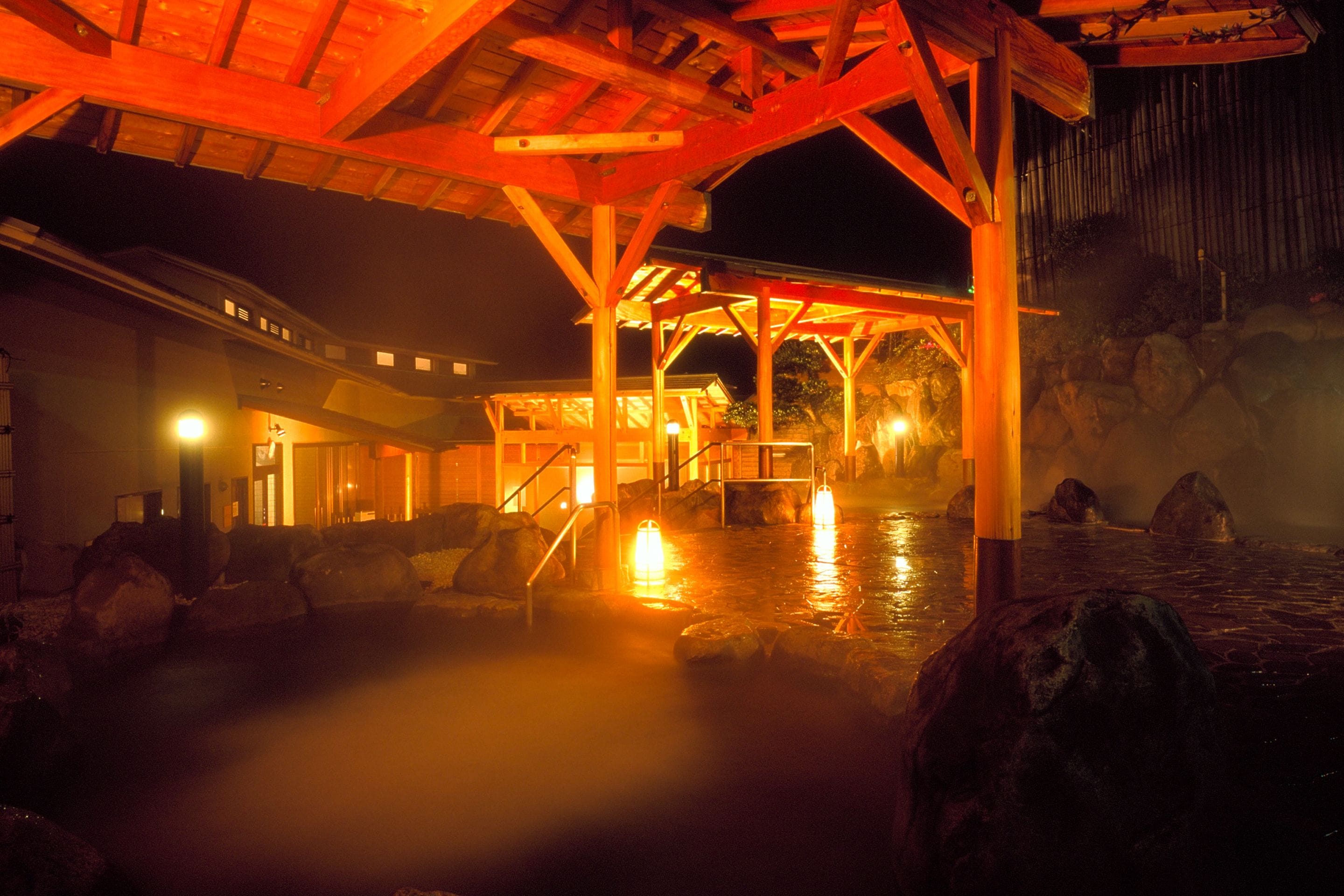 A traditional Japanese onsen with wooden structures and a stone bath area.