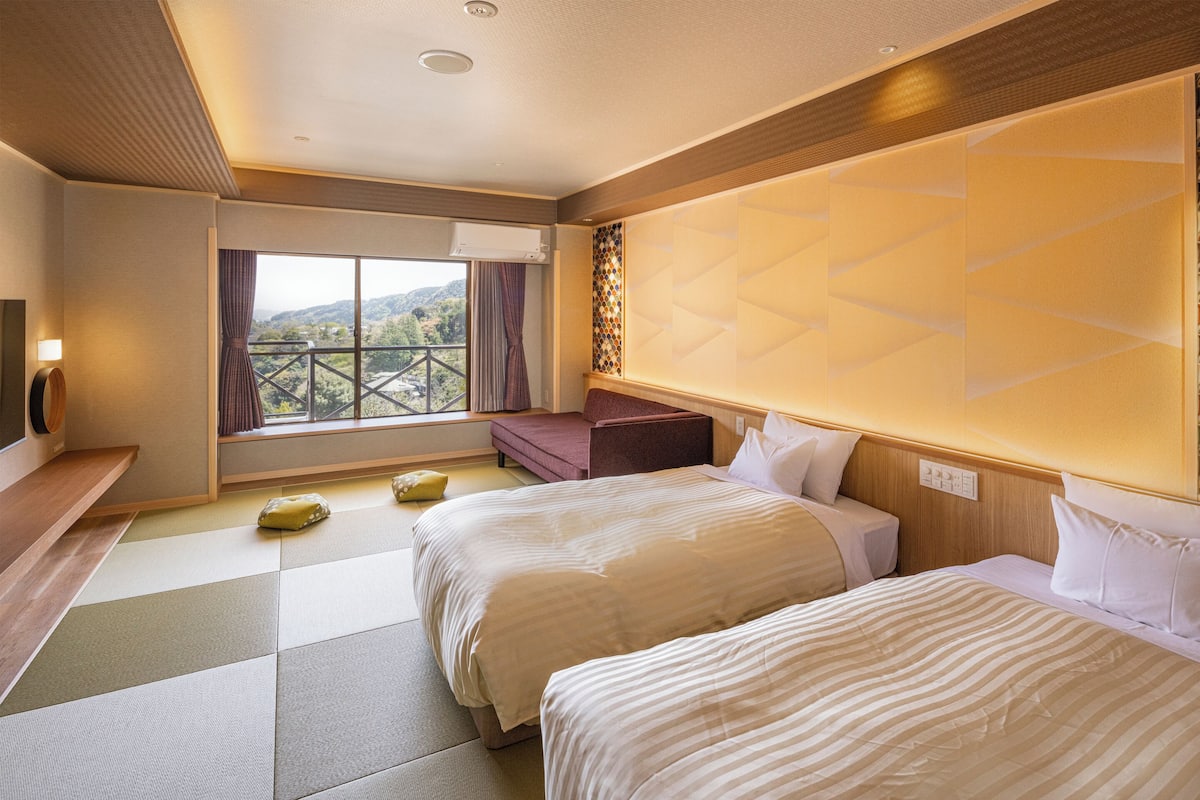Habitación de hotel con dos camas, un sofá, una ventana con vistas y un cabecero de madera.