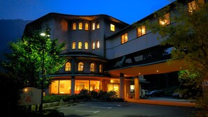A multi-story hotel with a curved facade, illuminated windows, and a covered entrance area. - Hakonenomori Okada (Hakone)