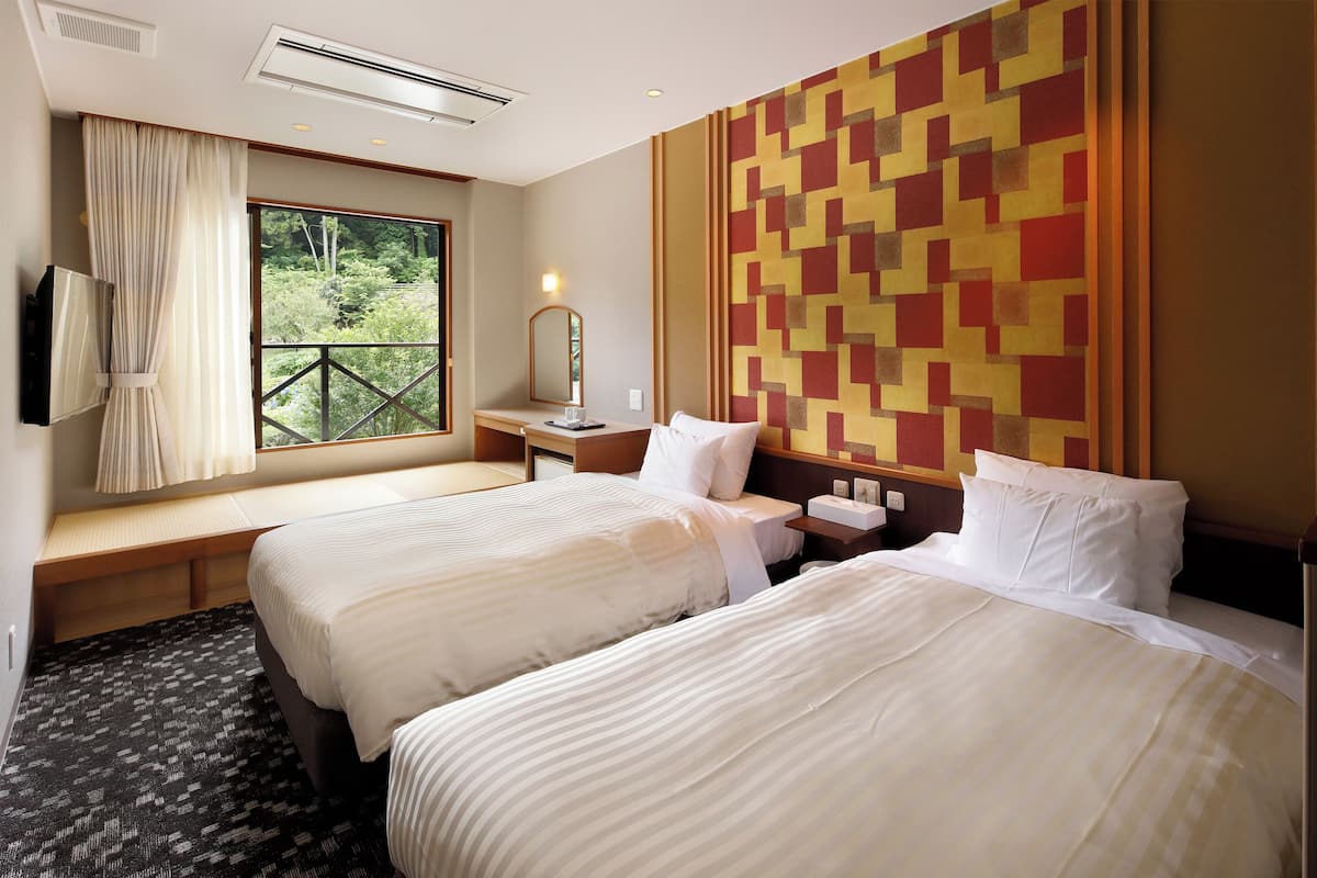 Habitación de hotel con dos camas, un ventanal con vistas a zonas verdes, televisor montado en la pared y un diseño de pared estampado.