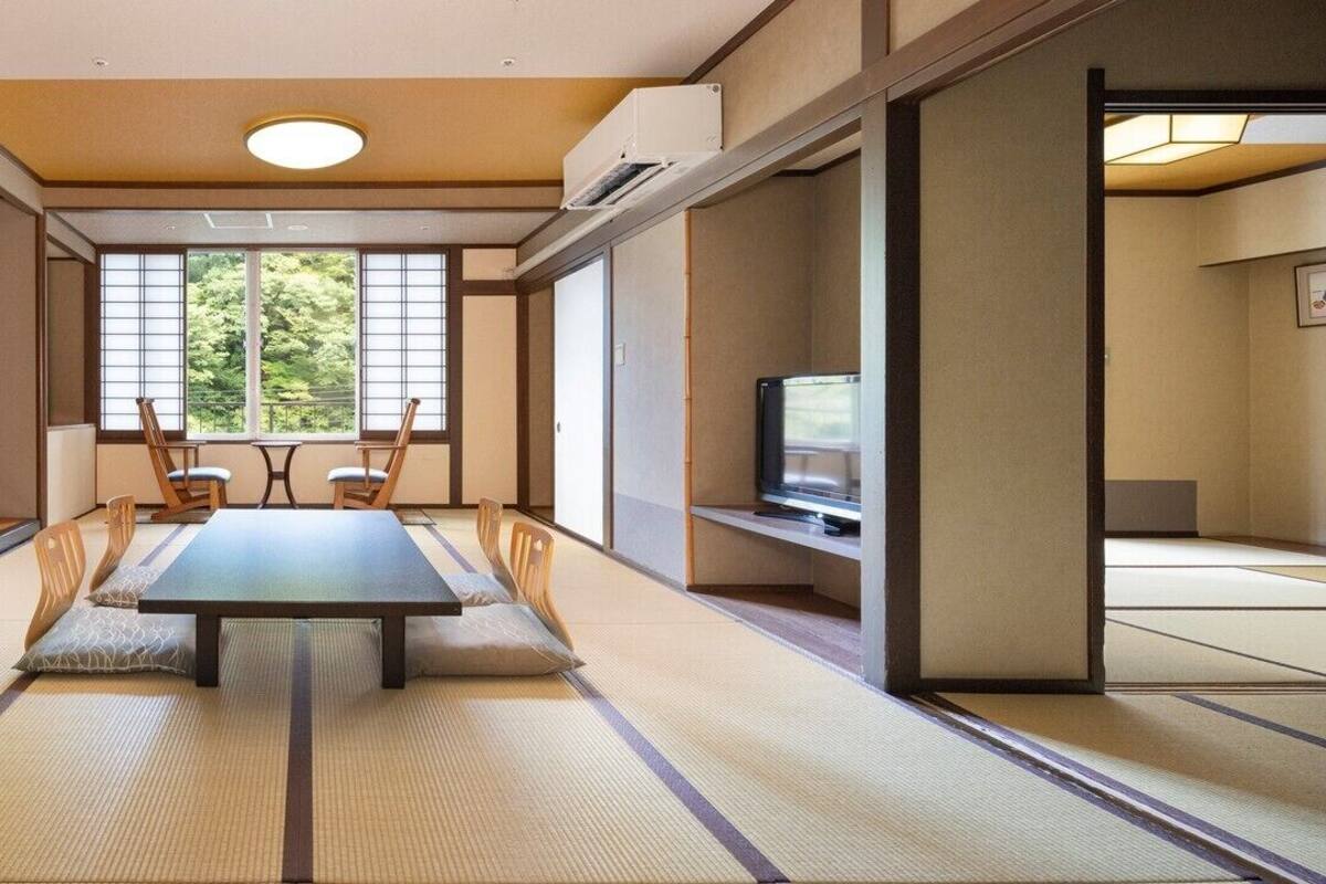 A traditional Japanese room with tatami flooring, a low table with cushions, sliding doors, and a television.