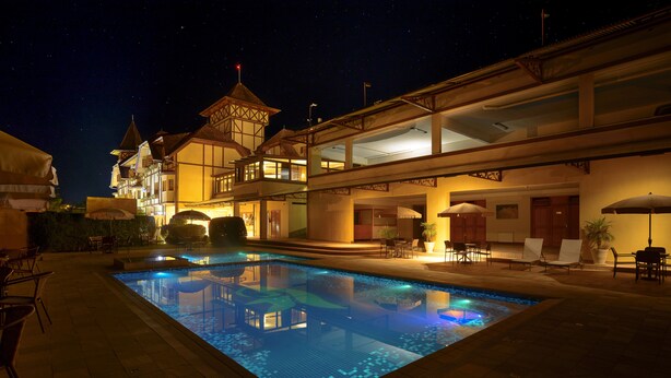 Una piscina con una fuente de agua azul cristalina, rodeada de mobiliario exterior y un edificio de estilo arquitectónico tradicional.
