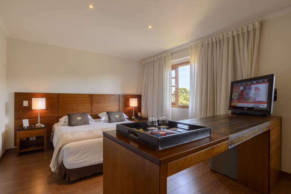 Ein Hotelzimmer mit Bett, Nachttischen, einem Fernseher und einem Tablett mit Gläsern.