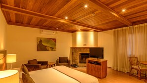 Una habitación de hotel con una cama grande, una chimenea, un televisor y un rincón comedor con sillas.