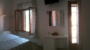 Ein Zimmer mit einem Bett, einem kleinen Nachttisch, einem Spiegel und einem Fenster mit Vorhängen.