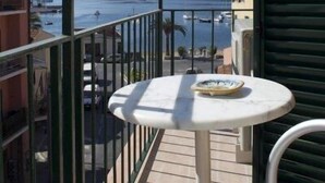 Ein Balkon mit Tisch und Stühlen, der auf einen Yachthafen mit Booten und eine hügelige Landschaft blickt.