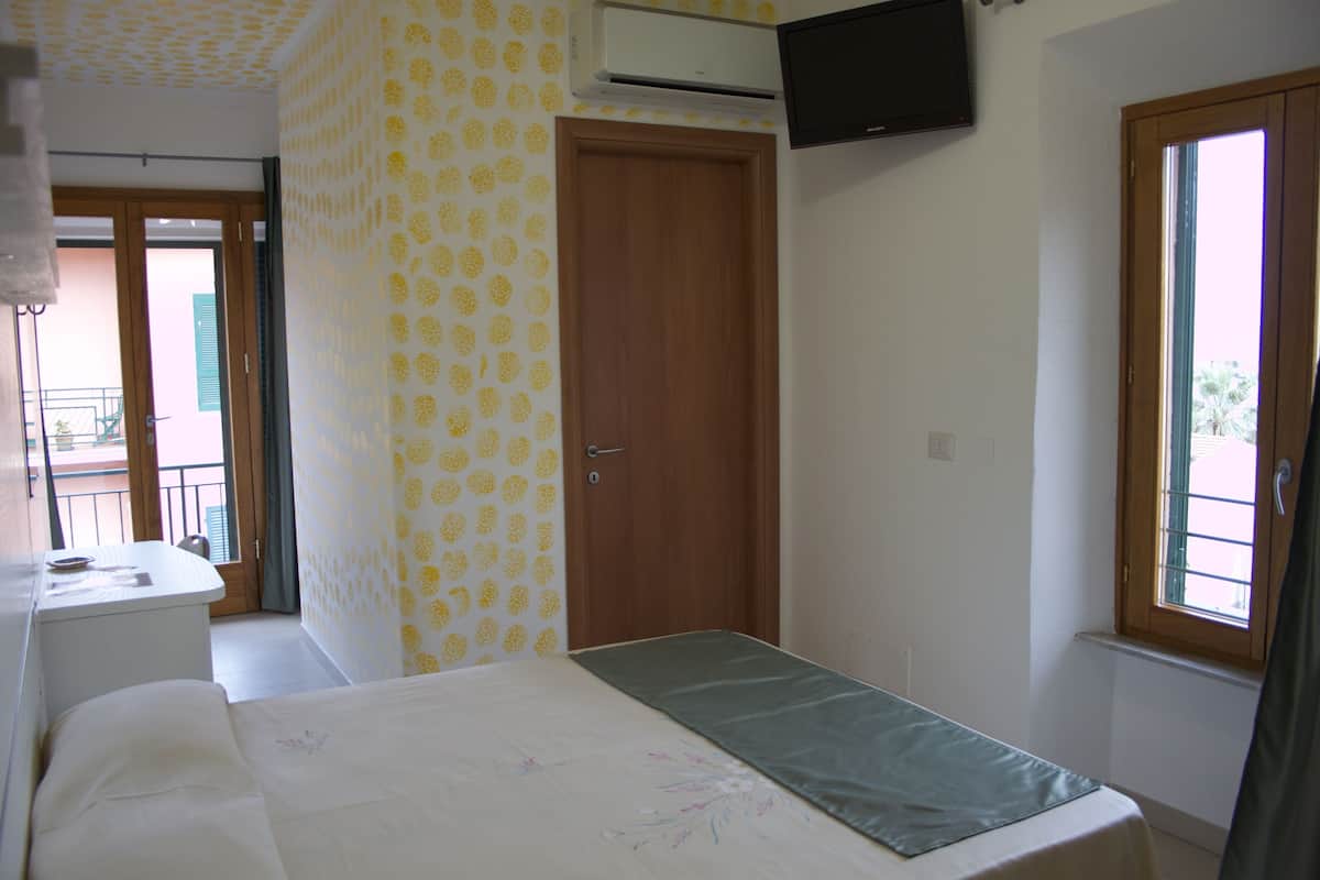 Une chambre à coucher avec un lit, un téléviseur fixé au mur, une fenêtre et une porte.