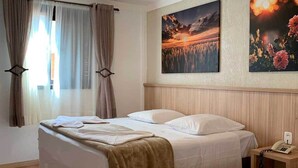Habitación de hotel con dos camas, un ventanal con cortinas, un cuadro de un atardecer y un teléfono en la mesita de noche.