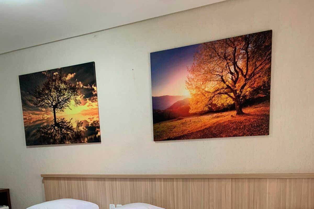 A hotel room with two beds, a wooden headboard, and two paintings of trees on the wall.