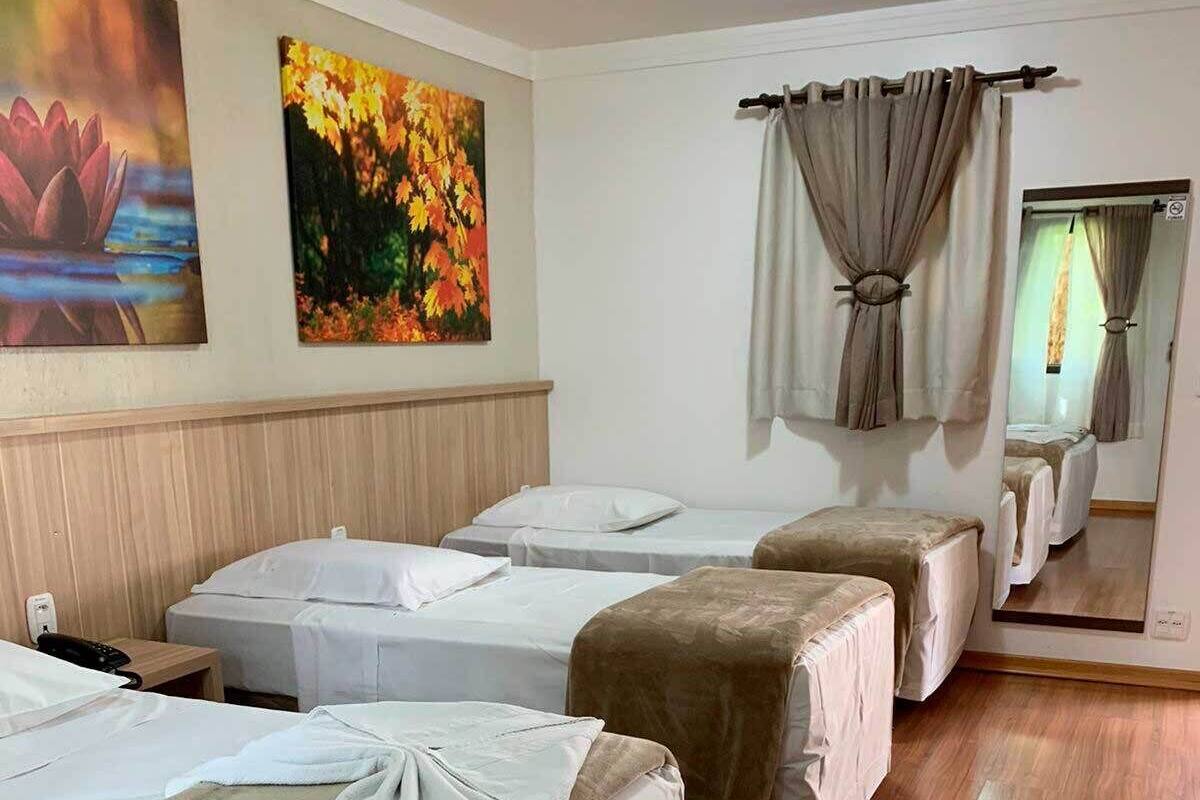 A hotel room with three beds, a wooden floor, and two paintings on the wall.