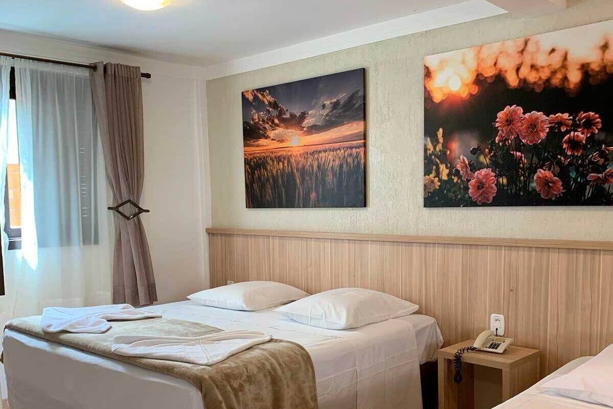 A hotel room with two beds, a wooden headboard, a nightstand with a phone, and two wall-mounted paintings.