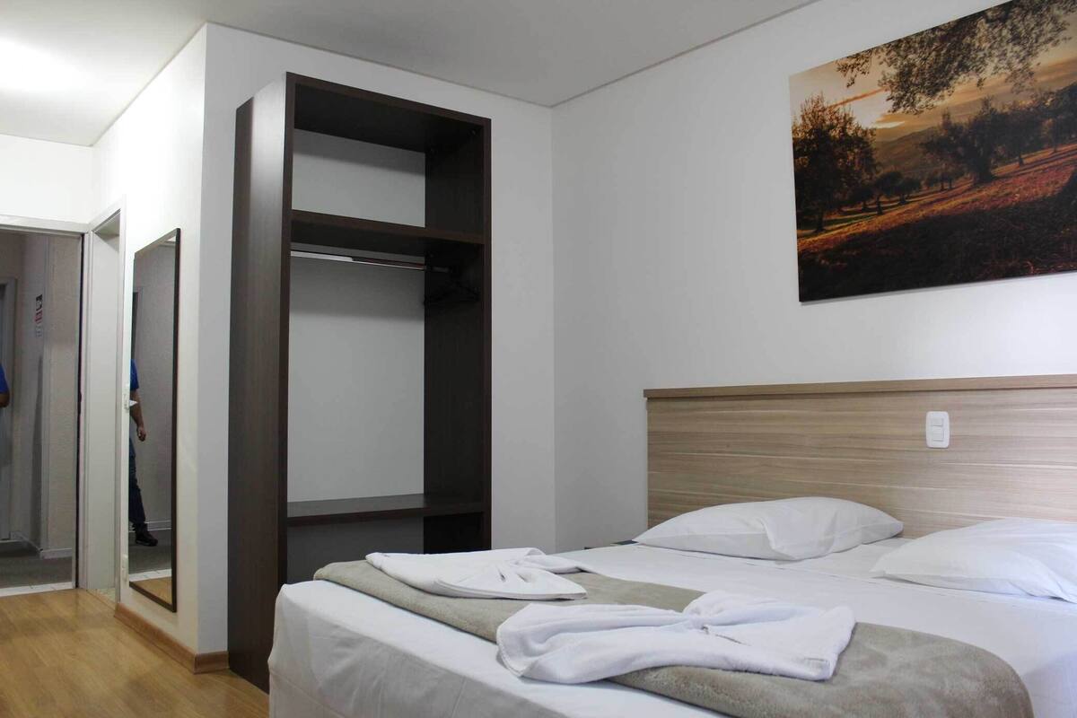 A hotel room with a bed, a wardrobe, and a painting on the wall.