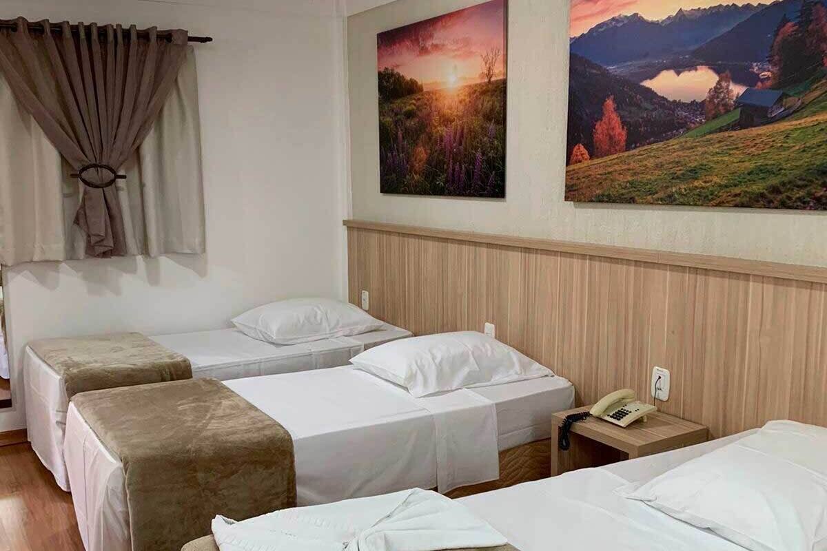 A hotel room with four beds, a wooden headboard, a painting of a sunset, and a telephone on the nightstand.