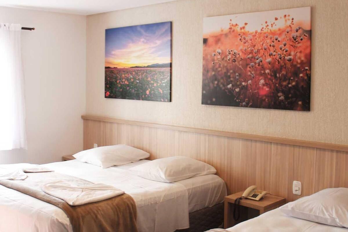 A hotel room with two beds, a wooden headboard, a nightstand with a phone, and two wall-mounted paintings.