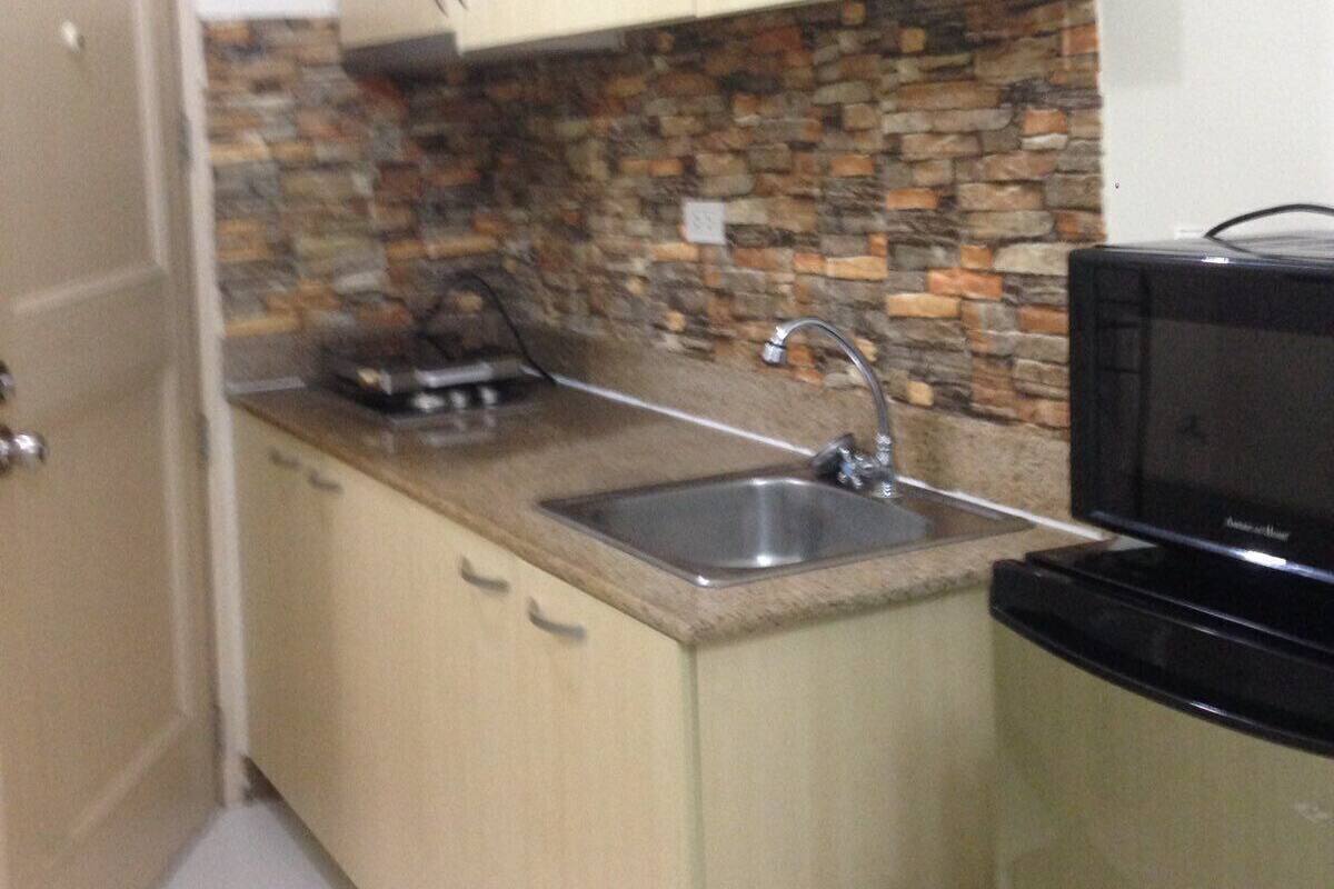A kitchen with a stone backsplash, a sink, and a microwave.