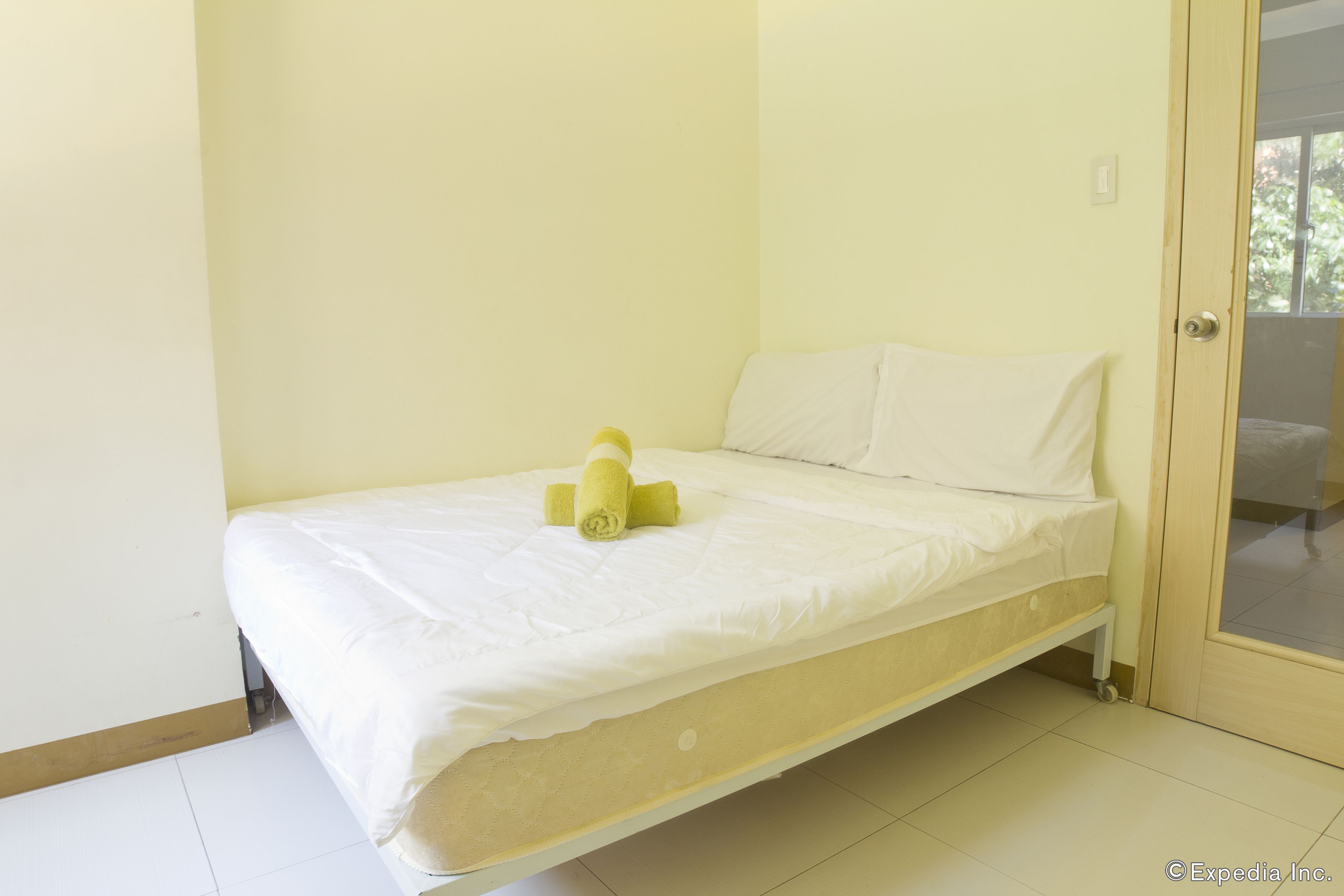 A single bed with a white mattress and a yellow towel rolled up at the head.