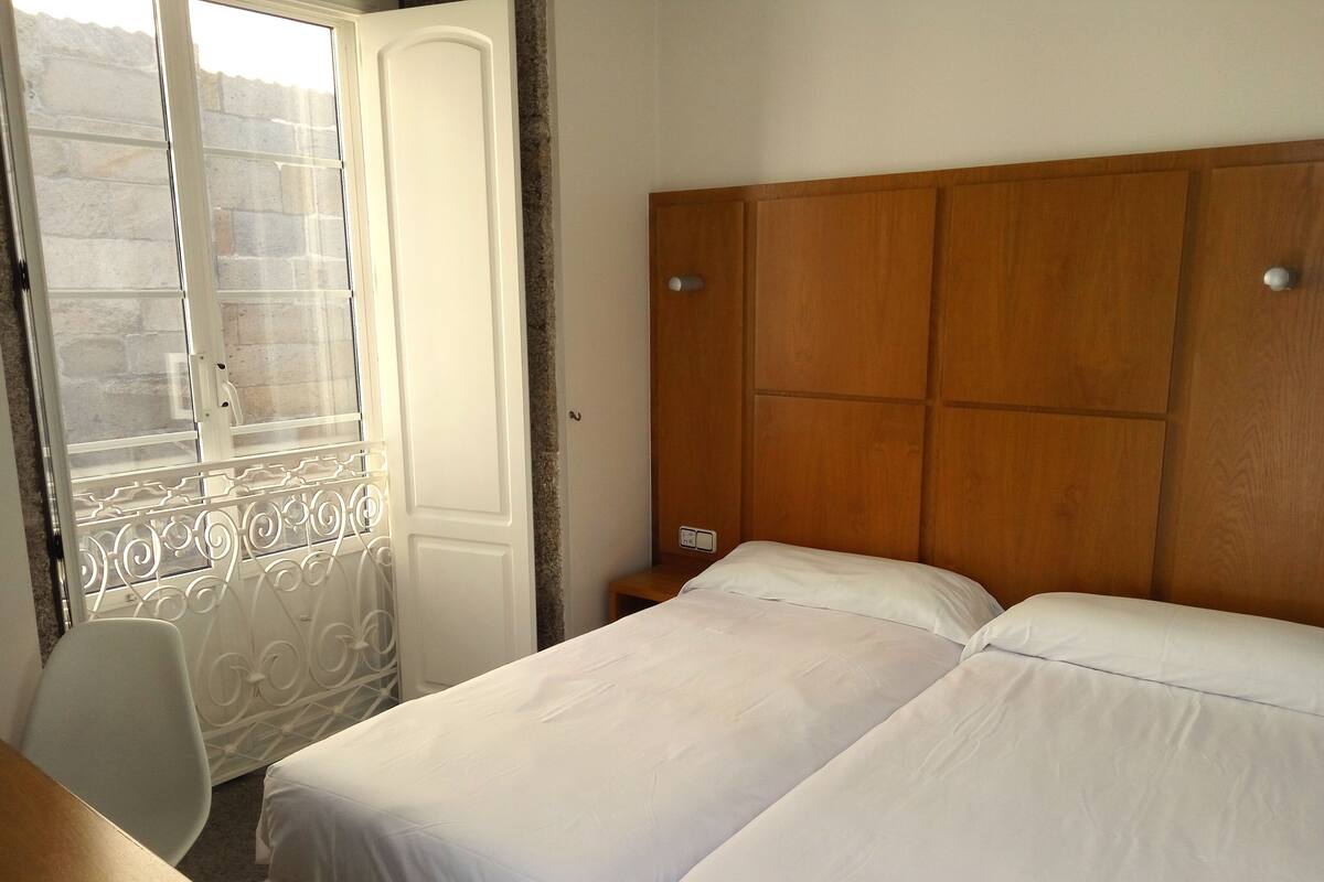 Une chambre à coucher avec une tête de lit en bois, un lit recouvert de draps blancs, un bureau et une chaise.