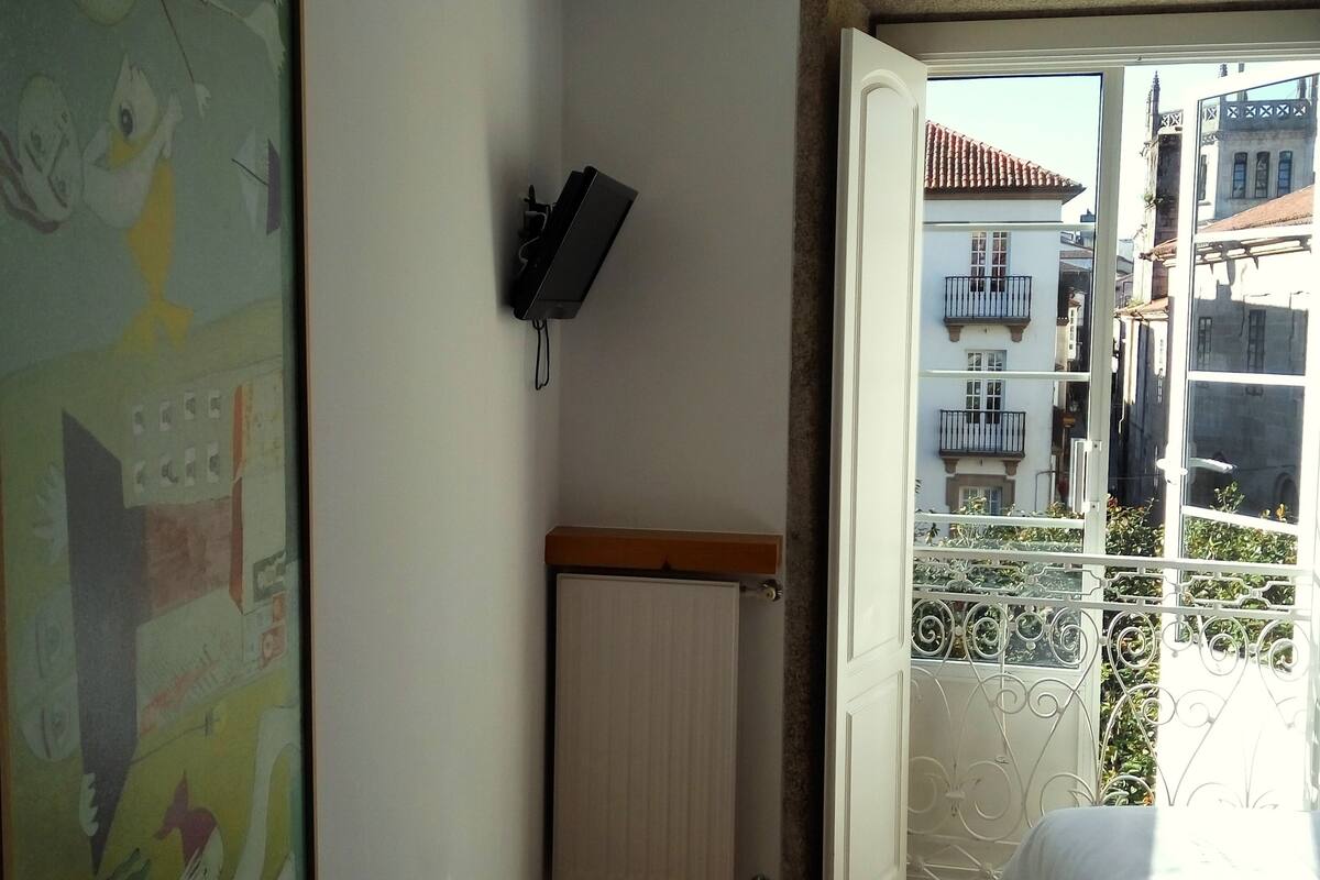 Une pièce avec un plancher en bois, un radiateur, un téléviseur fixé au mur et un grand tableau abstrait.