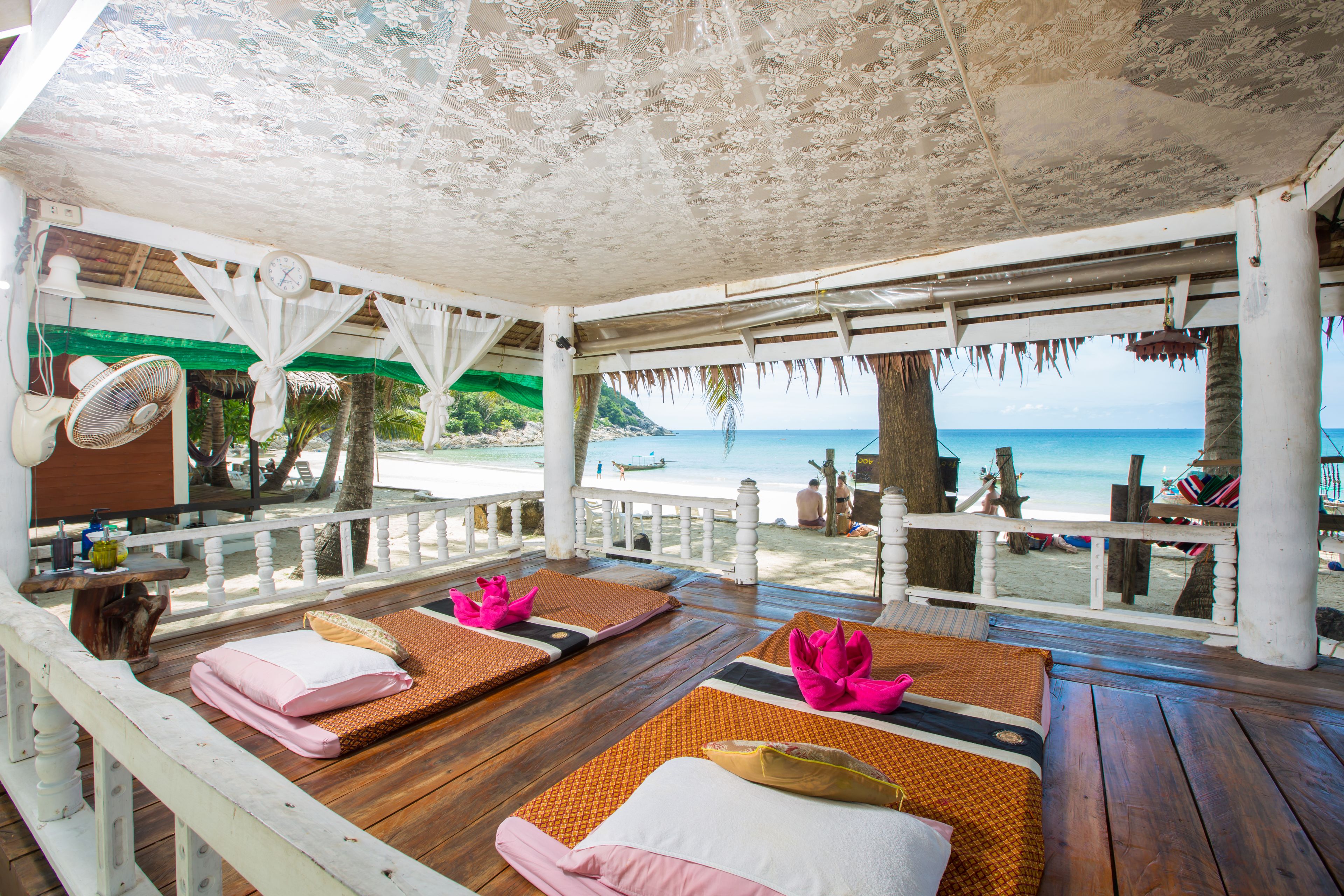 A beachside lounge with wooden flooring, cushioned seating, and a view of the ocean.