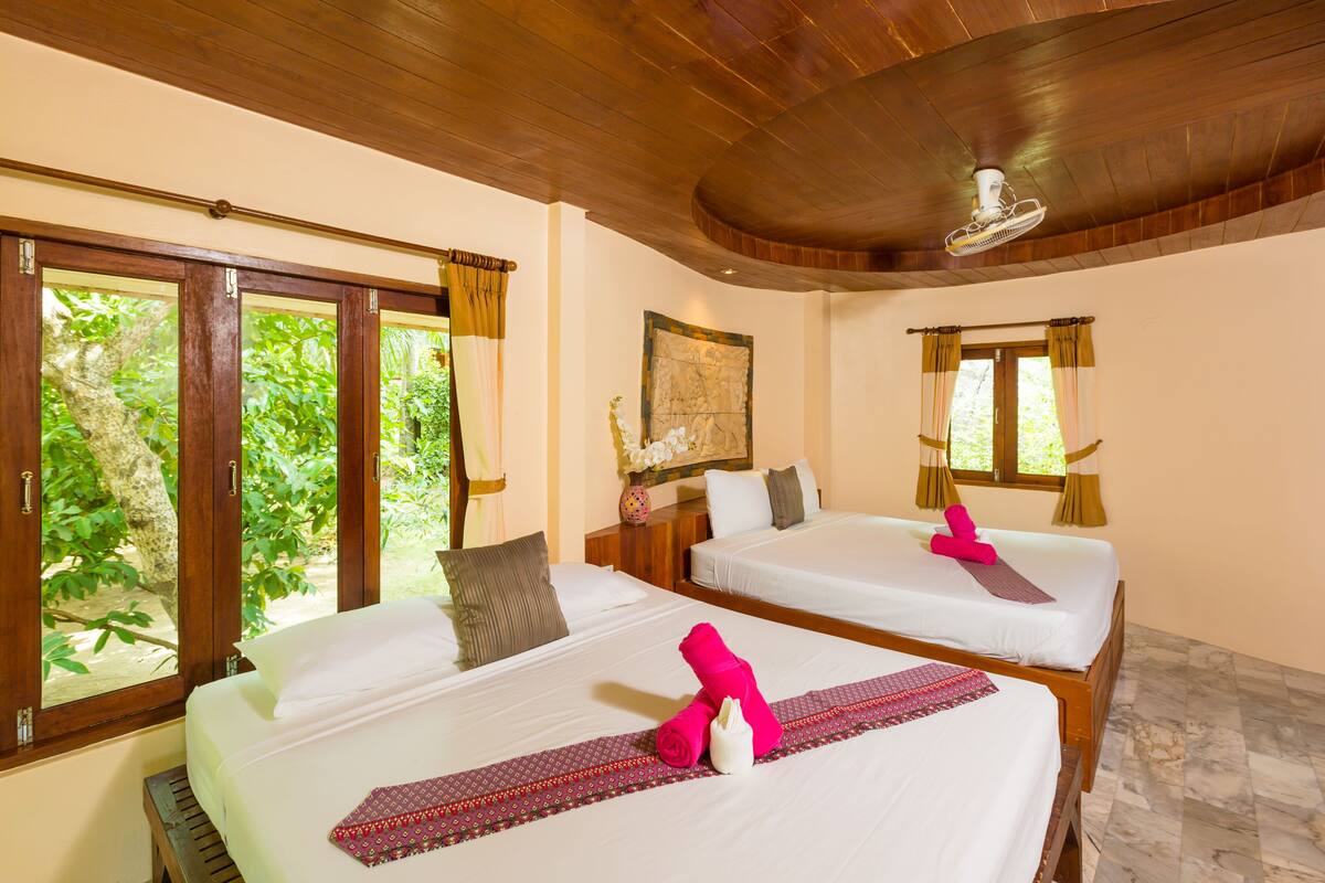 Two double beds with white linens, a wooden ceiling, and a window with curtains.