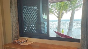 A room with a wooden desk, a window with a view of the sea and palm trees, and a patterned curtain. - Bottle Beach 1 Resort (Ko Pha-ngan)