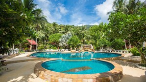 A large outdoor swimming pool surrounded by palm trees and a stone wall. - Bottle Beach 1 Resort (Ko Pha-ngan)