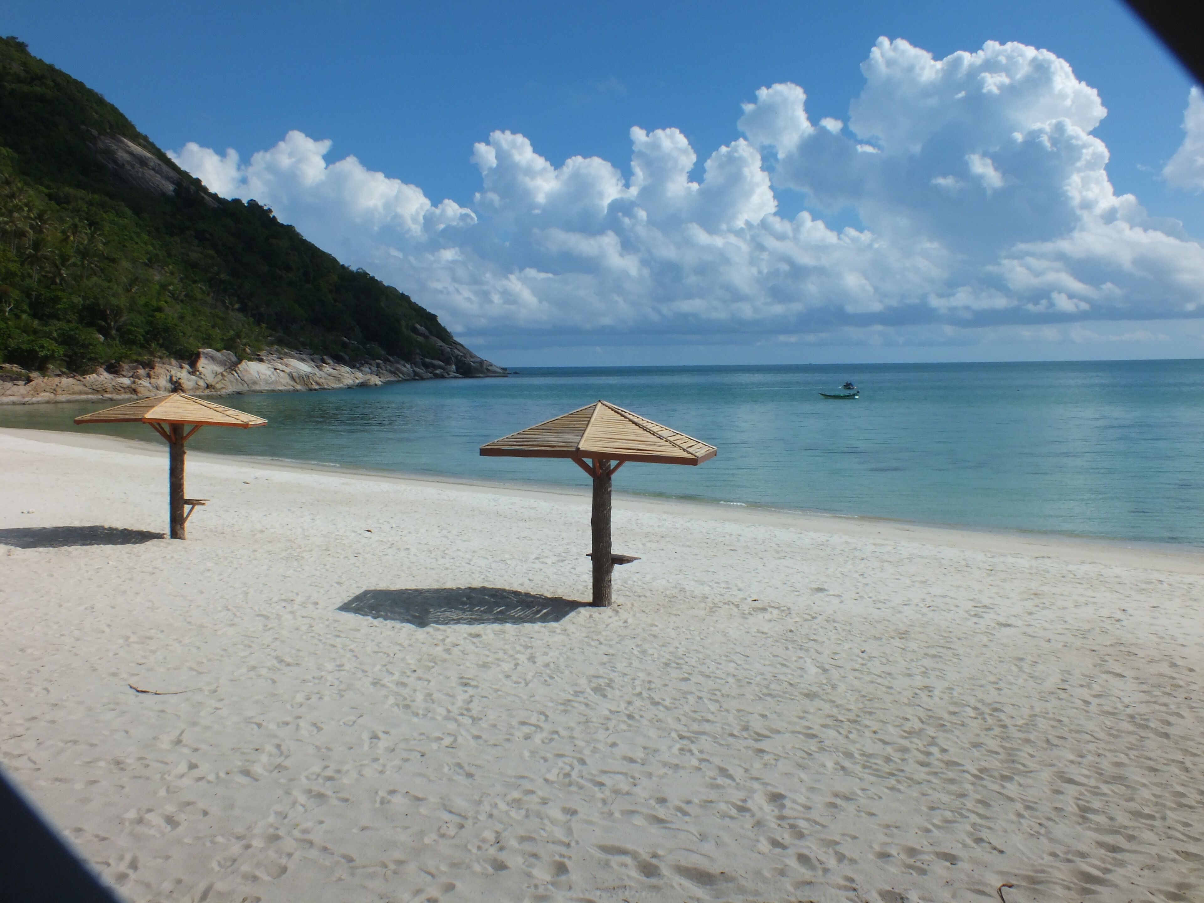 A beach with two wooden umbrellas and a clear view of the ocean.
