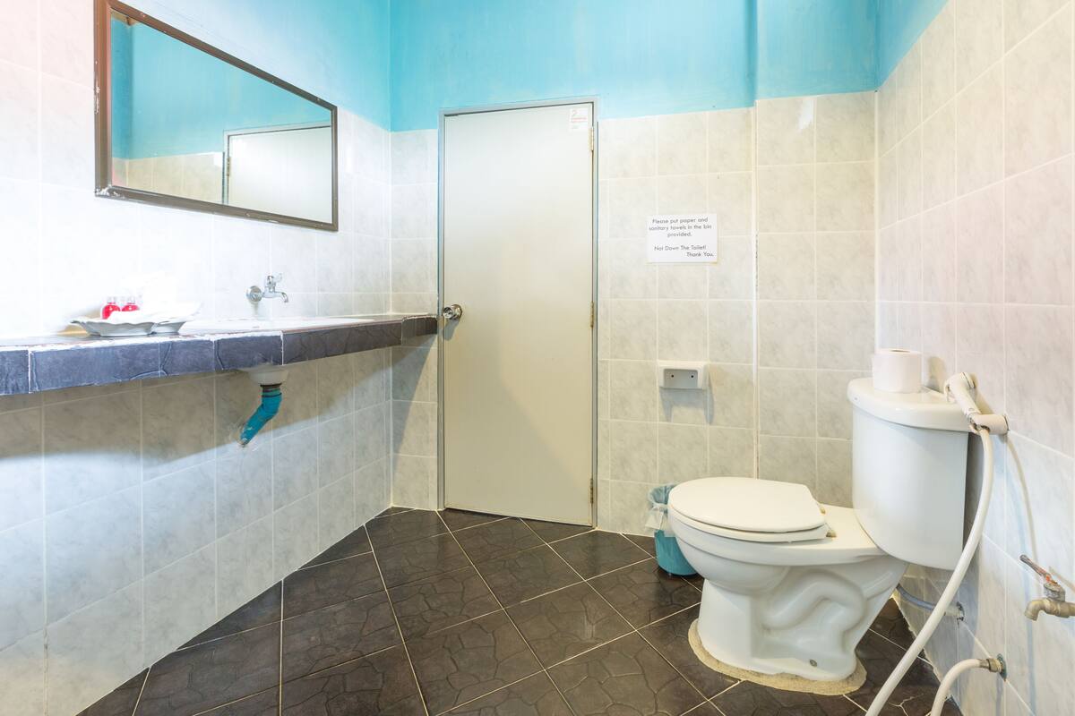 A bathroom with a toilet, sink, and mirror. There is a sign on the wall and a blue trash bin.