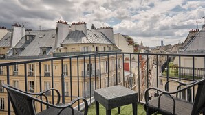 Un balcón con mobiliario de mimbre y vistas a un paisaje urbano con edificios históricos.