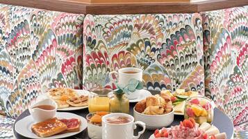 Zona pranzo con un divano dal motivo colorato, un tavolo rotondo con articoli per la colazione e un elemento decorativo a parete.