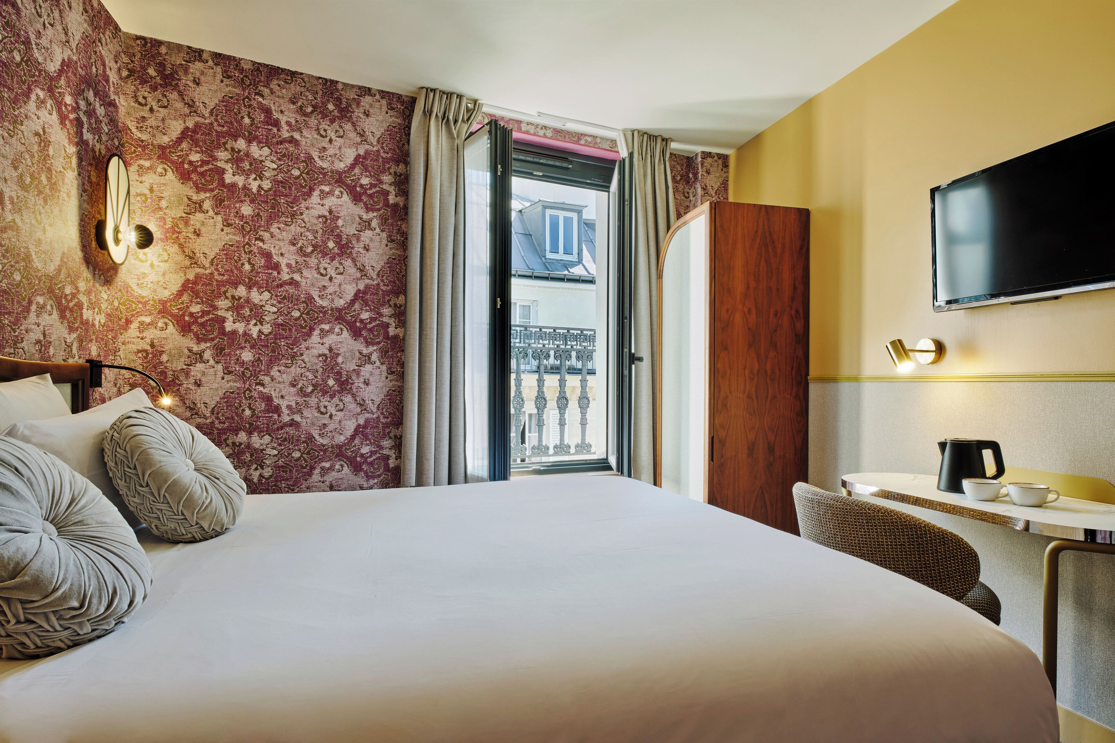 Camera d'albergo con un letto grande, una scrivania con sedia, una TV a schermo piatto e vista su un balcone.