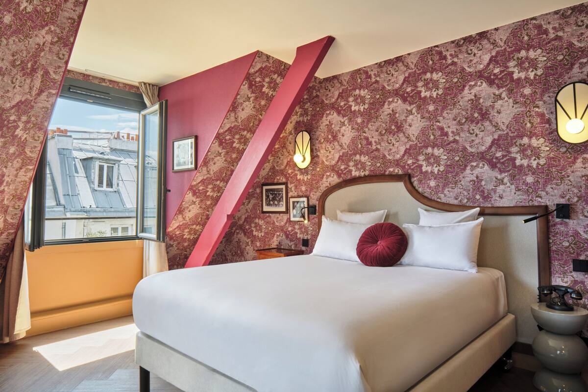Un dormitorio con una cama grande, una ventana con cortinas, un reloj de pared y una mesita de noche con lámpara.
