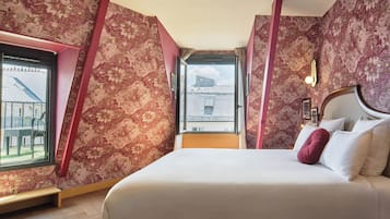 Ein Schlafzimmer mit einem großen Bett, floralem Wandpapier, einem Fenster mit Blick auf Gebäude und einem Nachttisch mit Lampe.