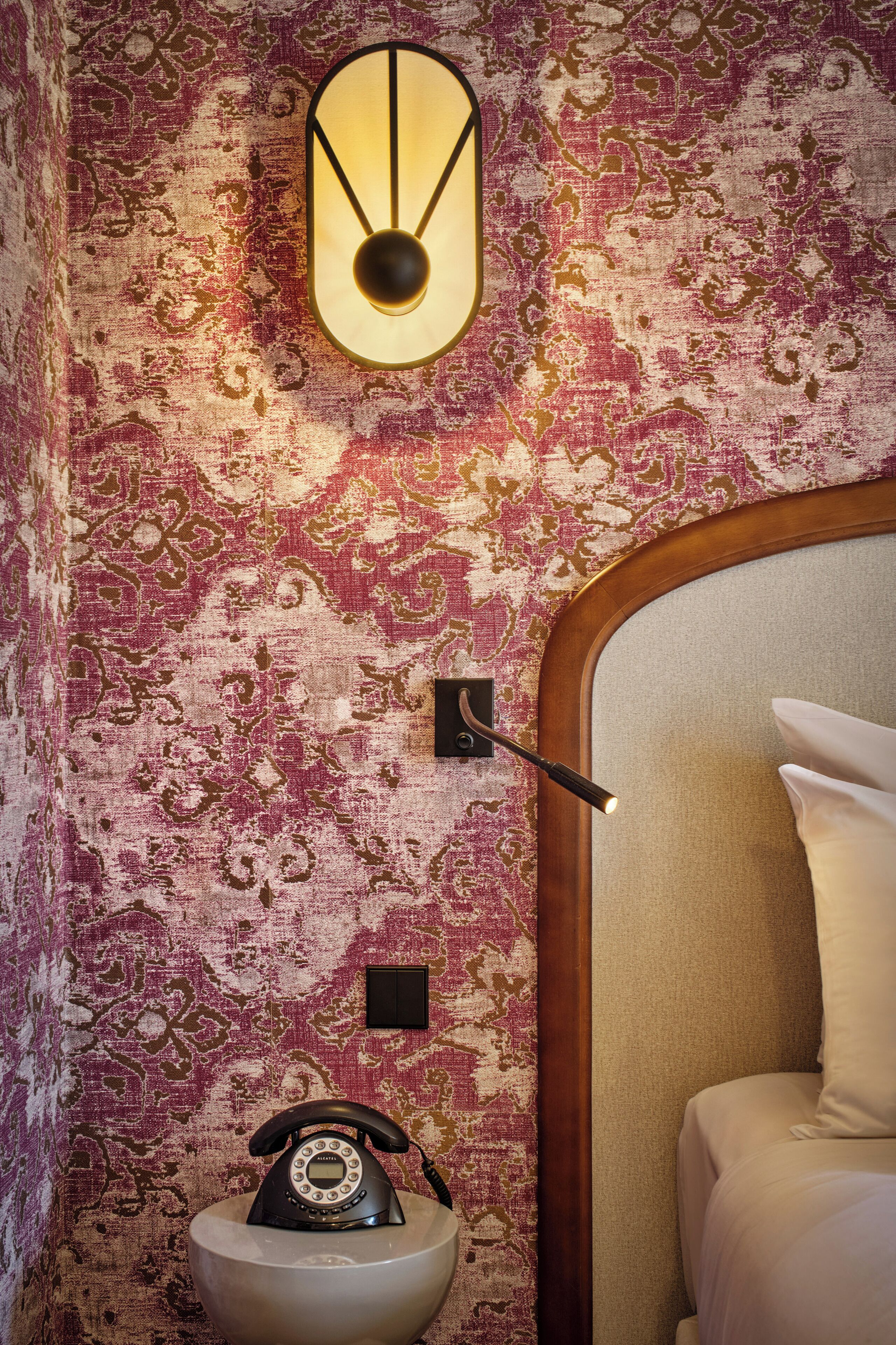Una stanza con carta da parati decorata, un lampadario a parete, un telefono e un letto con cuscini.