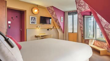 A hotel room with a large bed, a desk with a chair, a flat-screen TV mounted on the wall, and a window with a view of the outside.