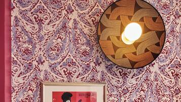 A wall with a patterned wallpaper, a framed poster, and a wall-mounted light fixture.