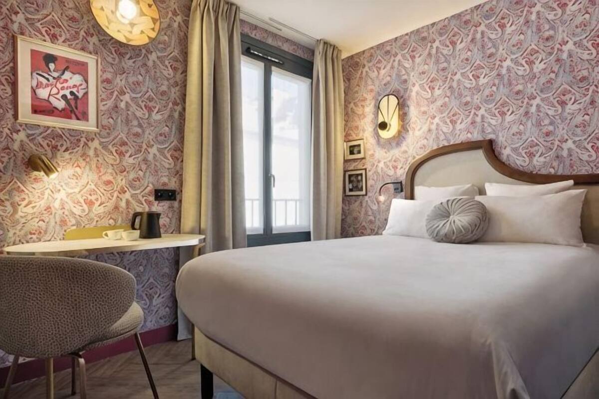 Una habitación de hotel con cama, escritorio, silla, ventana con cortinas y pared con diseño.