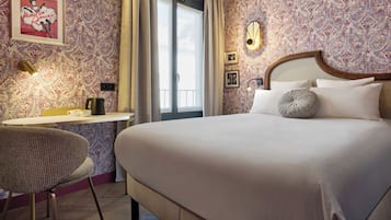 A hotel room with a large bed, a desk with a chair, a framed picture on the wall, and a window with curtains.