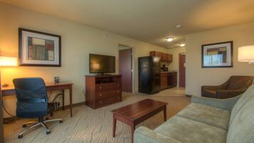 A hotel room with a sofa, a desk with a computer, a television, a refrigerator, and a kitchen area.