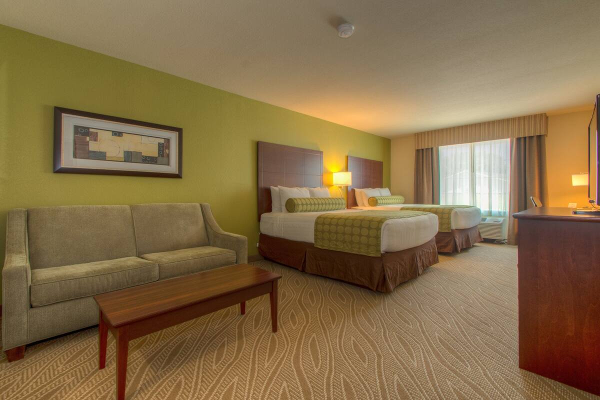 A hotel room with a sofa, two beds, a desk, and a framed picture on the wall.