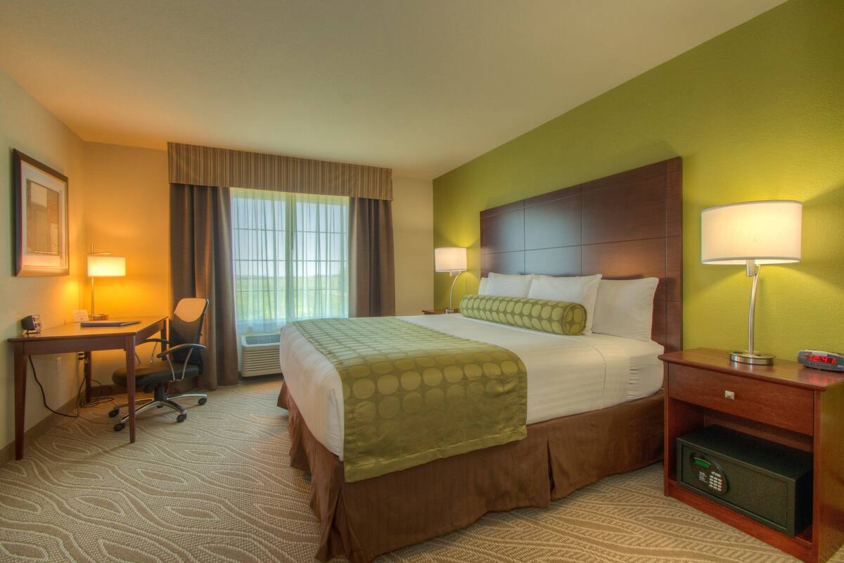 A hotel room with a bed, desk, chair, lamps, and a safe.