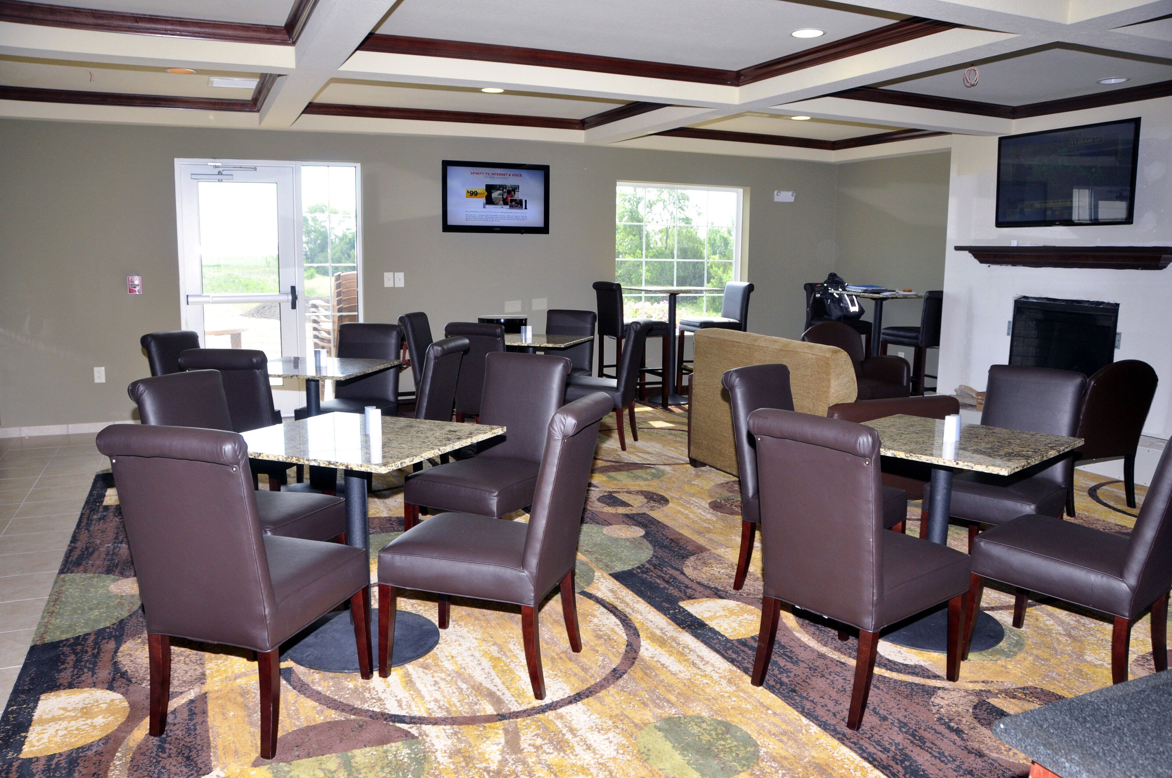 A hotel dining area with multiple tables and chairs, a fireplace, and a television on the wall.