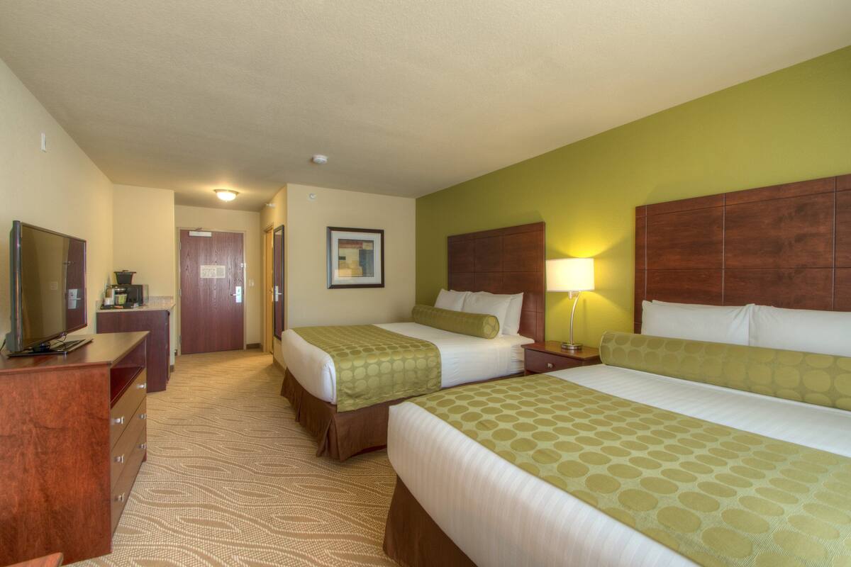 A hotel room with two beds, a desk with a TV, a wooden headboard, and a framed picture on the wall.