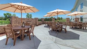 Un espace extérieur aménagé en terrasse, avec plusieurs tables et chaises, chacune agrémentée d’un parasol beige.