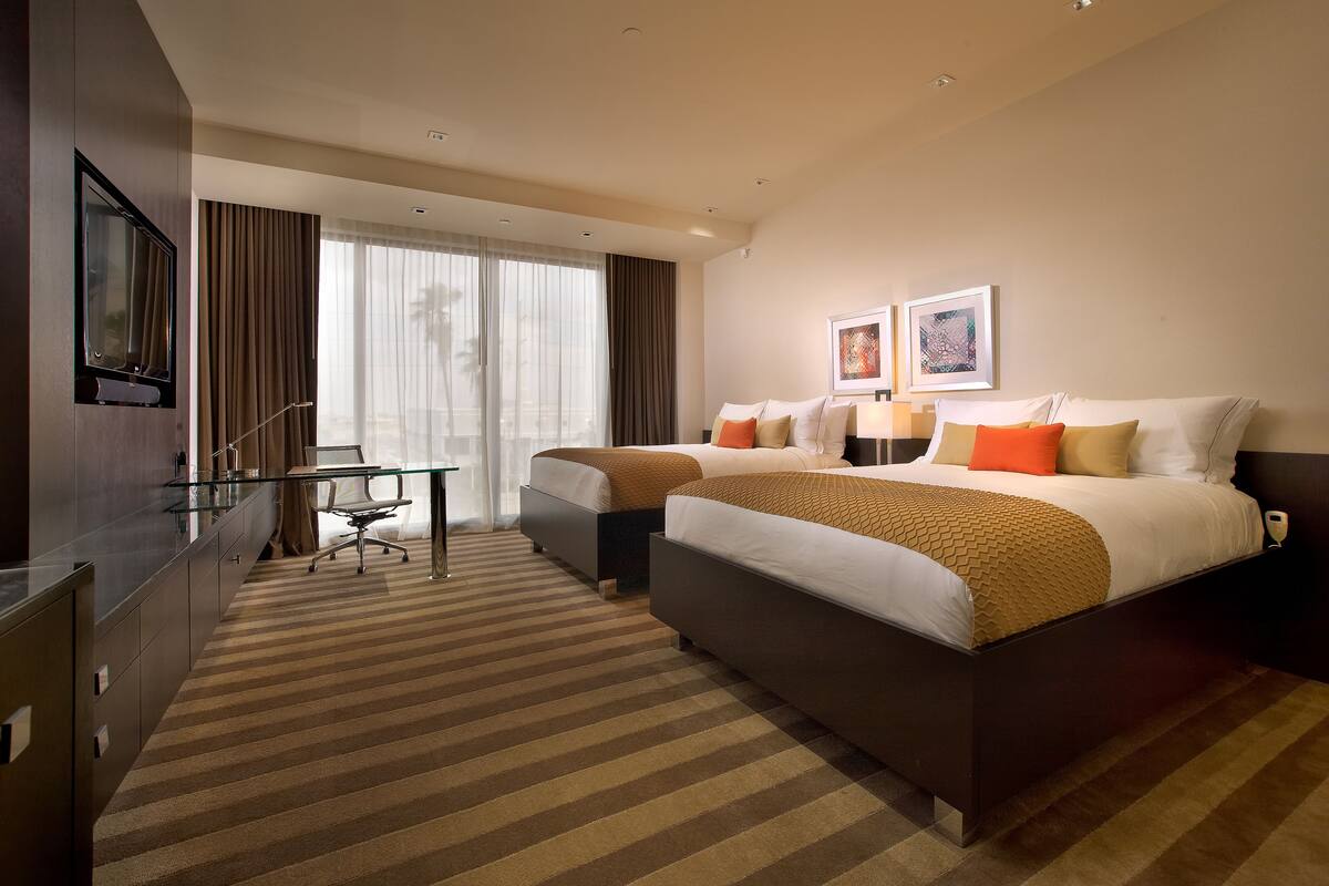 A hotel room with two beds, a desk, and a TV.