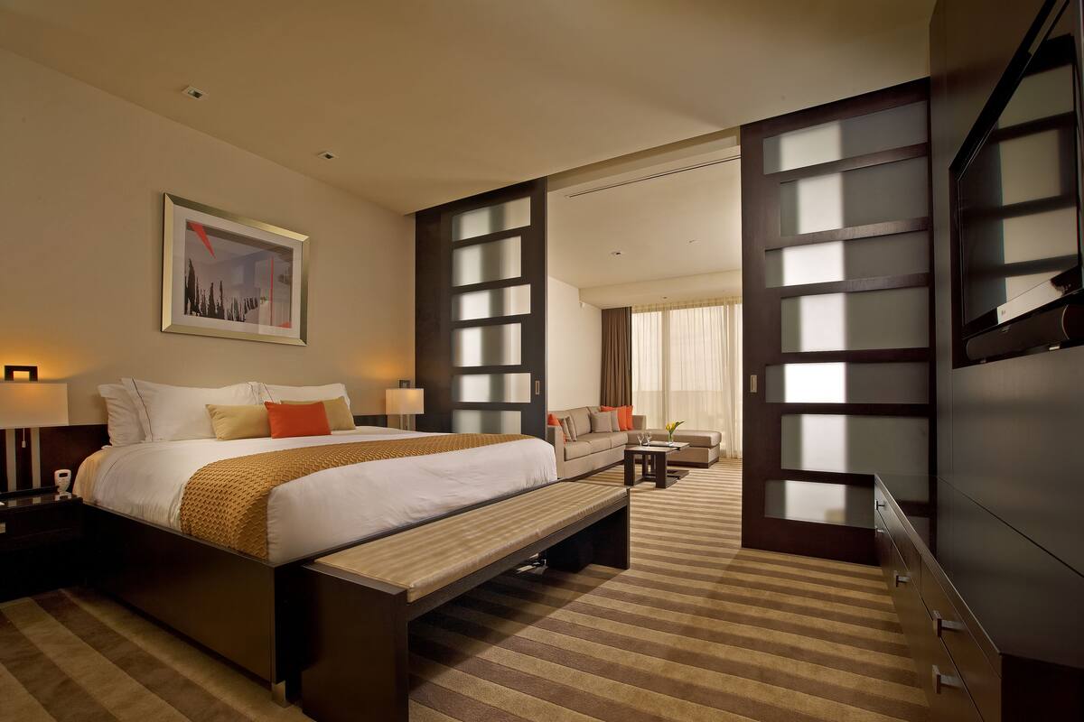 A hotel room with a large bed, a sofa, a desk, and a TV.