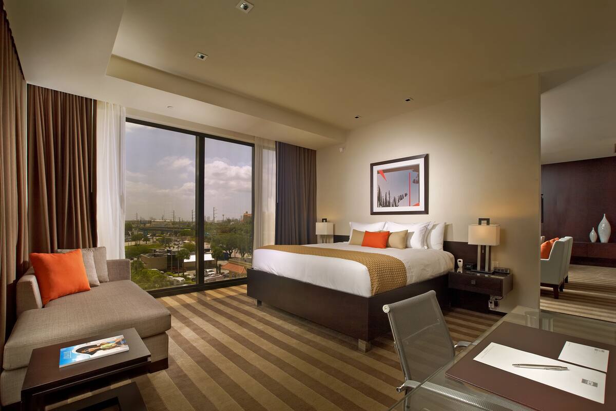 A hotel room with a large bed, a sofa, a desk, and a view of the city.