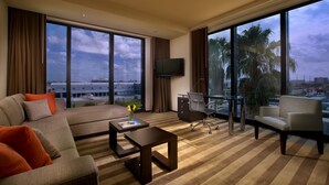 A modern hotel room with a large window, a sofa, a desk, and a chair.
