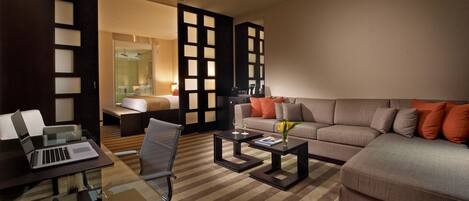 Una habitación de hotel moderna con sofá, sillón y una mesa de vidrio con una computadora portátil.